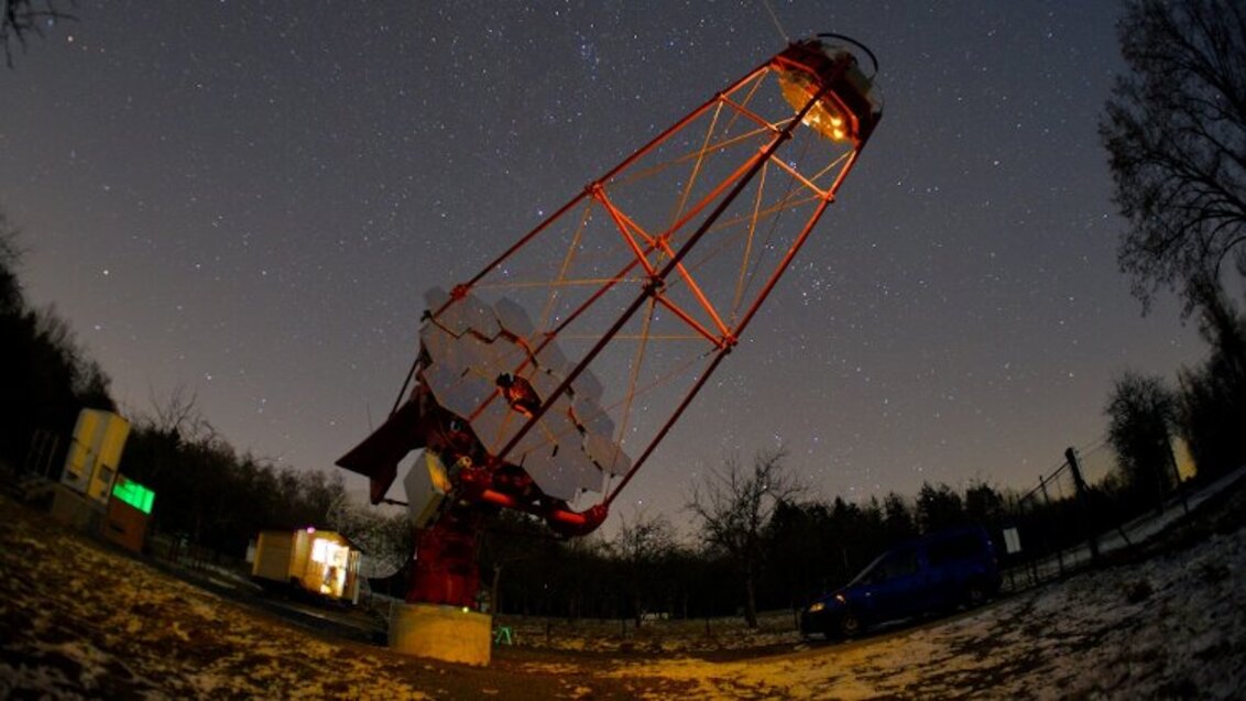 The photo shows one of the telescopes from the Cherenkov Telescope Array. It is directed towards the stars. The background constitutes a starry night sky.