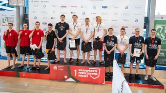 Na zdjęciu trzy męskie zespoły zawodników na podium (odpowiednio na 1, 2 i 3 miejscu). Na szyjach zawodników zawieszone są medale. Troje z nich (po jednym w każdej drużynie) trzyma w dłoniach pamiątkowy dyplom. Za zawodnikami ścianka z logotypami sponsorów zawodów.