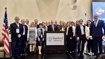 Grupowe zdjęcie przedstawicieli AGH. Stoją na scenie za mównicą z logo „Stanford University”. Po lewej stronie widoczna jest flaga Stanów Zjednoczonych oraz ekran z elementami graficznymi.