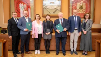 Grupa 7 stojących osób w sali konferencyjnej