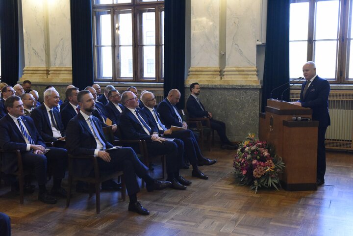 Guests seated in the Assembly Hall listen to a speaker at a lectern.