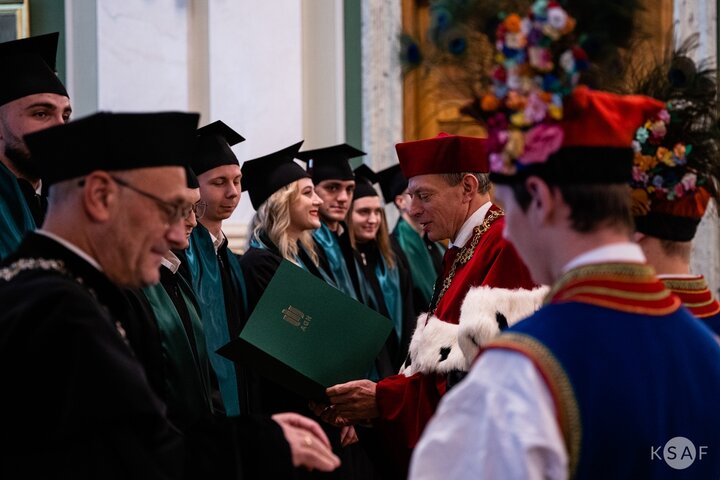 Image of a vice-rector in festive gown congratulating university alumni in togas and birettas while giving them congratulatory letters with some help from members of the University Song and Dance Ensemble Krakus