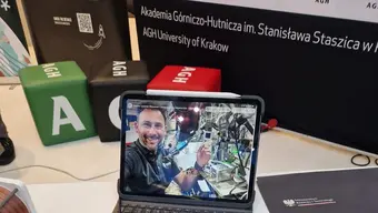 Ekran laptopa, na którym widać mężczyznę w przestrzeni kosmicznej. W tle kolorowe pufy AGH
