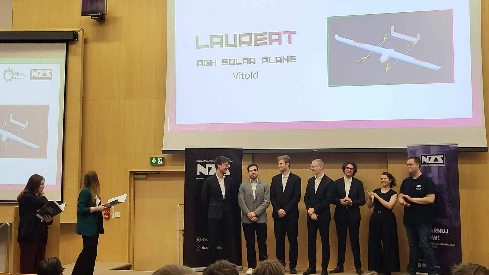 Członkowie zespołu AGH Solar Plane stoją na scenie podczas gali Konkursu KoKoS 2026. W tle widoczna jest prezentacja z napisem „LAUREAT” oraz grafika bezzałogowego statku powietrznego VITOLD.