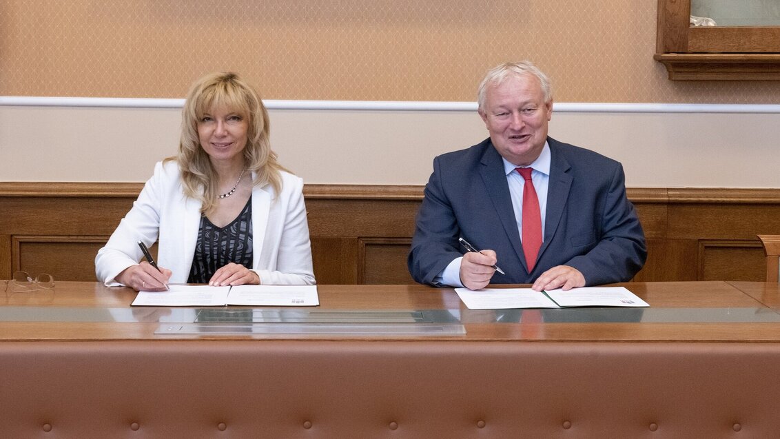 Na zdjęciu sygnatariusze umowy - siedzą za stołem, przed nimi dokumenty z umową, w dłoniach trzymają długopisy. Zdjęcie wykonane w sali konferencyjnej AGH.