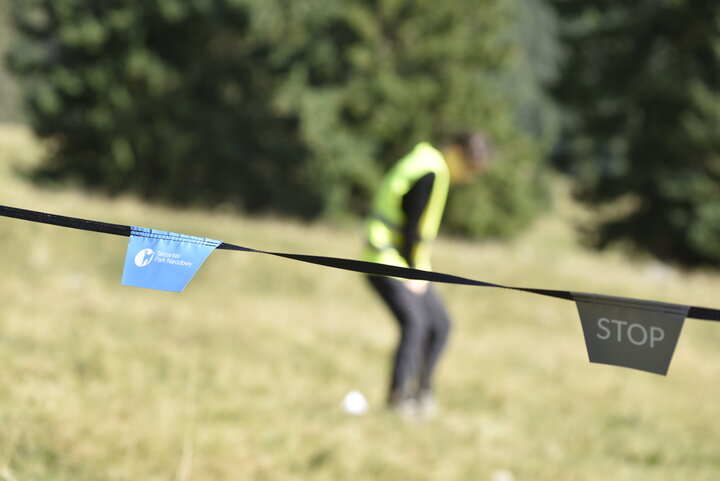 Blurred person in the background on a grassy field, with a rope or tape in the foreground displaying a "STOP" tag and a tag of the Tatra National Park.