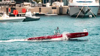 Remote-controlled racing boat speeding across the water near a marina.