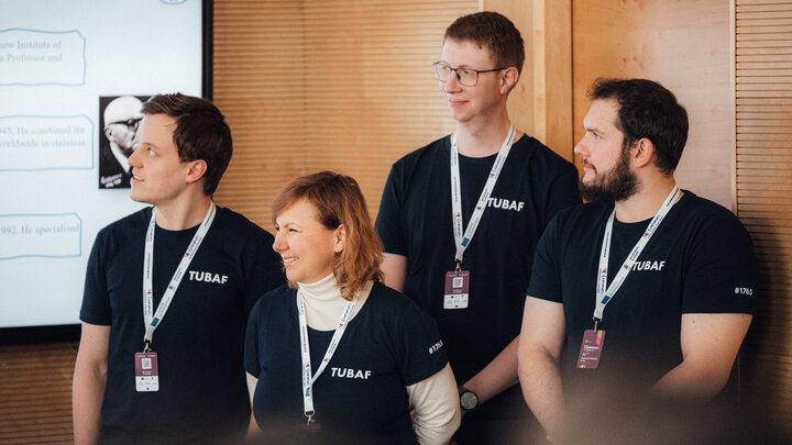 Image of a group of people standing next to a presentation screen dressed in the same t-shirts from TU Bergakademie Freiberg; each person has a badge from the Erasmus+ event