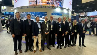 Grupa dziesięciu elegancko ubranych osób, uczestników targów, na tle multimedialnego baneru