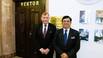The rectors of AGH University and GGSIPU stand in the reception hall in front of a door marked “Rektor”. Next to the door is an information board with the name of the AGH University of Krakow and the name of the rector. Portraits of previous rectors of the university are visible on the wall.