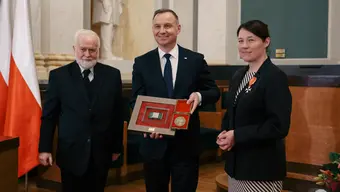 Three people pose for a photo. From the left: two men and a woman. The man in the middle holds a commemorative medal and a framed integrated circuit.