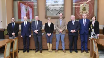 Grupa osób (dwie kobiety, sześciu mężczyzn) pozuje do wspólnego zdjęcia. Wszyscy stoją w rzędzie przed stołem prezydialnym w sali konferencyjnej. 