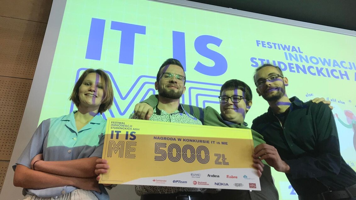 Zespół projektowy SaferVision. Cztery osoby trzymają przed sobą duży bon z z napisem 5000 zł. W tle na ekranie wyświetlony jest slajd z festiwalu IT IS ME..