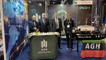 Stoisko Akademii Górniczo-Hutniczej na targach BALTEXPO, z widocznymi materiałami promocyjnymi, modelami technologicznymi oraz makietą jednostki pływającej „Barka” na stoliku z flagą AGH.
