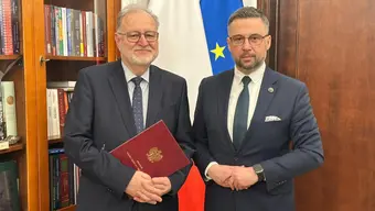 Prof. Kąkol (po lewej) i minister Kulasek (po prawej) stoją obok siebie w gabinecie ministerialnym. Prof. Kakol trzyma w dłoniach bordową teczkę.