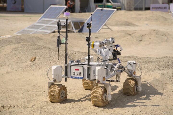 Photo of the rover Kalman moving on a sandy terrain with solar panels visible in the back.