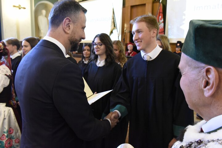 The Minister congratulates the newly enrolled student. Standing beside him is the smiling Rector.