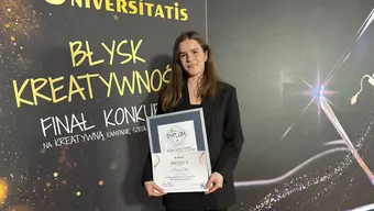 A young woman in a black suit posing against a dark-coloured competition backdrop holding a framed diploma.