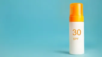 A white bottle of SPF30 sunscreen with an orange cap agains a blue backdrop.
