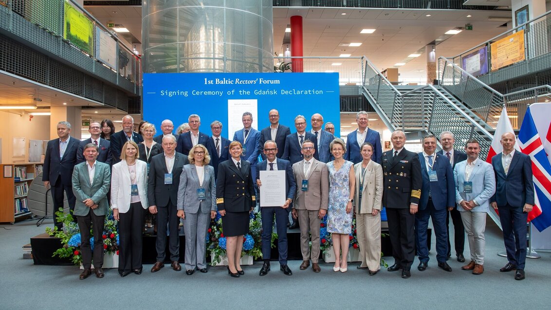 Group photo at the 1st Baltic Rectors’ Forum during the signing ceremony of the Gdańsk Declaration, with attendees standing in front of a blue event backdrop in a modern indoor atrium.