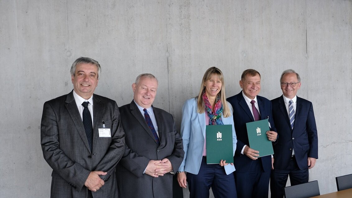 Five people in a row, smiling. Two of them hold green folders with the AGH university logo.