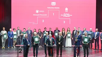 Photo from the award ceremony of the Academic Sports Gala. On a huge stage, the representatives of the three best universities are present. A row of people behind them. In the background, there is a gigantic pink screen that features an outline of a podium with the three best universities placed on the appropriate step of the podium.