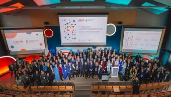 A group photograph of conference participants on stage in an auditorium taken from above.