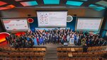 A group photograph of conference participants on stage in an auditorium taken from above.