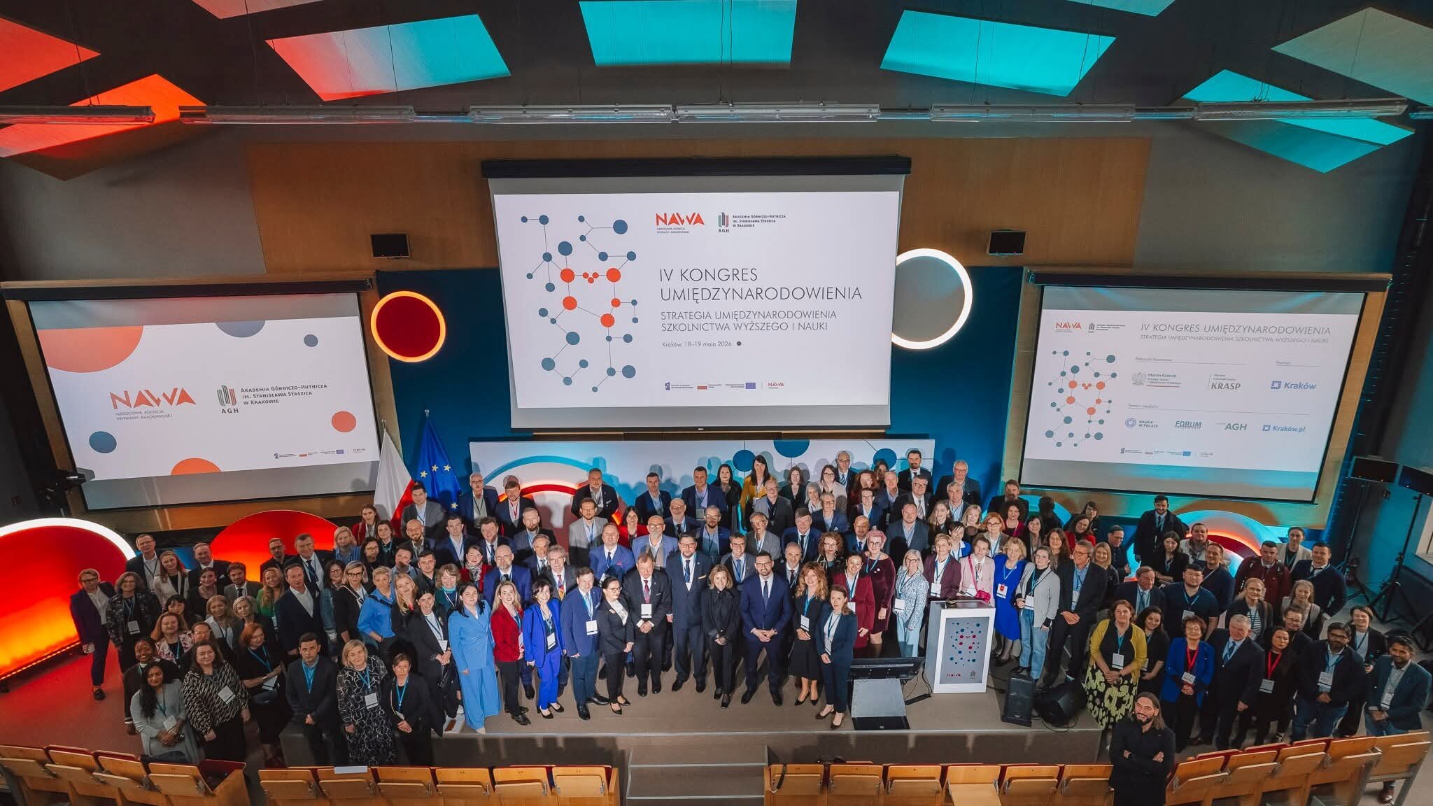 Grupowe zdjęcie uczestników i uczestniczek kongresu - stoja obok siebie na dużym podium, za nimi ekrany ze slajdami.