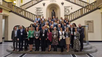 Image of a group of people standing in a hall on stairs in front of a statue