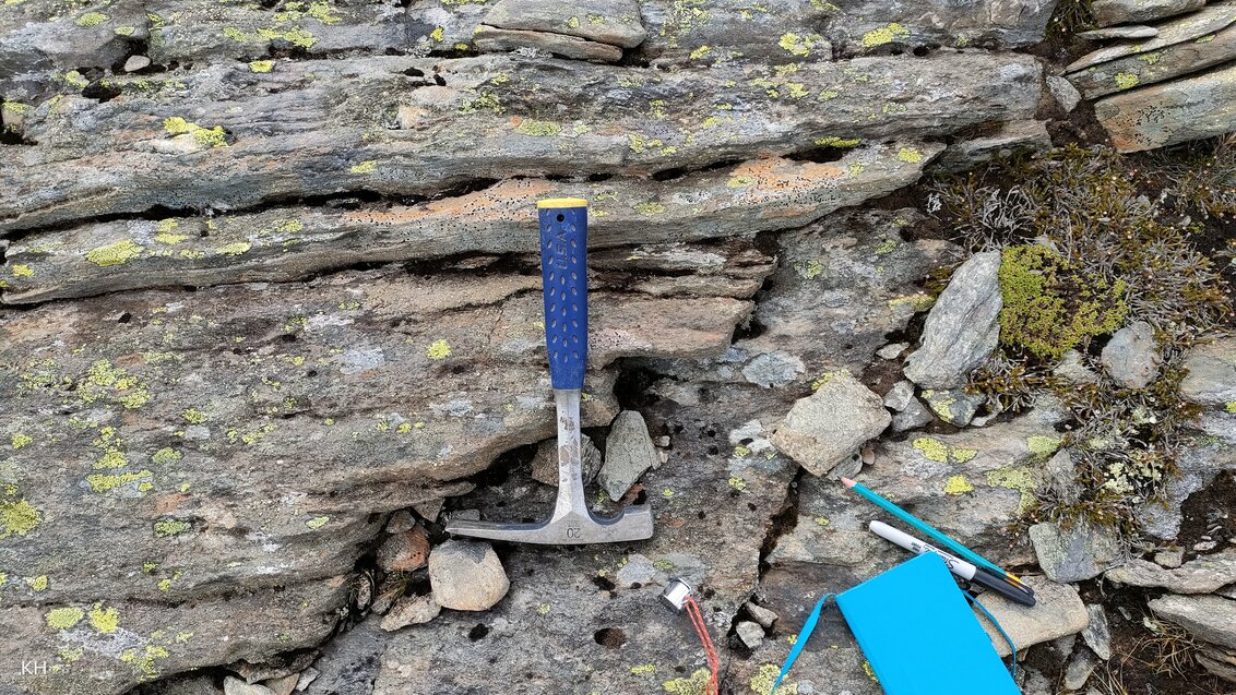 Na skalistym podłożu leży sprzęt do pracy w terenie, min. młotek, ołówki, notes.