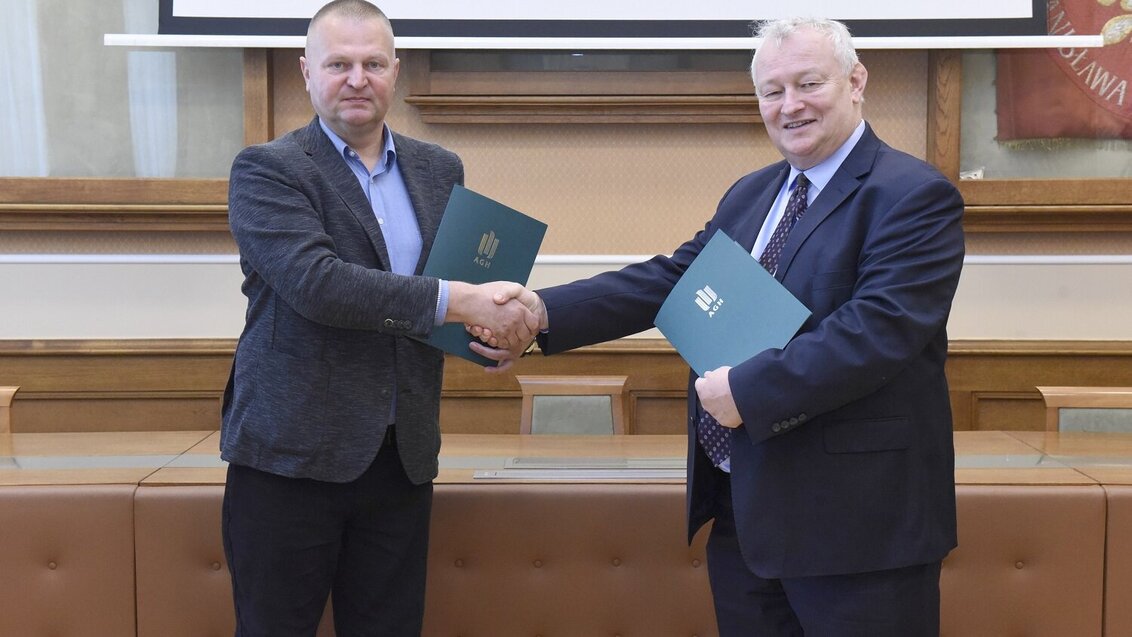 The photo shows two men shaking hands. They hold document files with the AGH UST logo.
