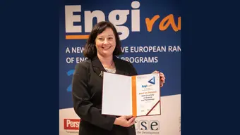 Image of the AGH University spokesperson holding a folder with a diploma in front of an EngiRank photo wall