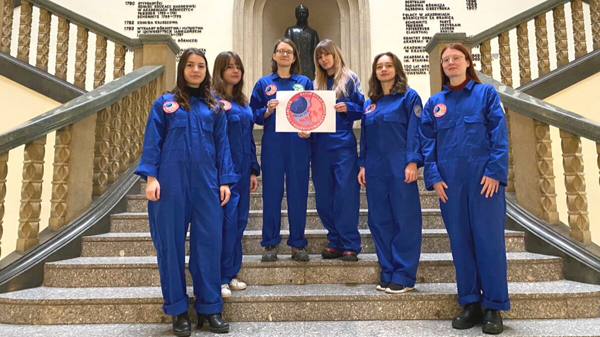 Mission participants dressed in blue astronaut uniforms. The photo was taken in the hall of the Main Building on a large staircase.