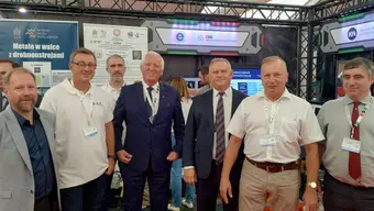Grupa 7 stojących mężczyzn w hali wystawienniczej.