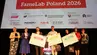 Eight people on a stage at the “FameLab Poland 2026” final, with three winners holding large prize checks under a banner with event details and sponsor logos.