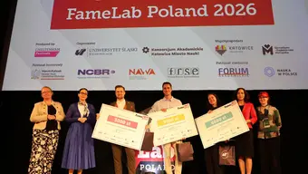 Eight people on a stage at the “FameLab Poland 2026” final, with three winners holding large prize checks under a banner with event details and sponsor logos.