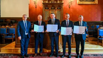 Zdjęcie grupowe: pięć osób prezentuje podpisane dokumenty w reprezentacyjnej sali