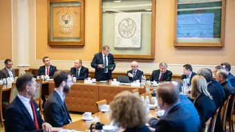 Photo from a meeting of a large group of people with tables in the U shape.
