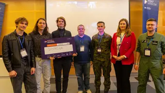 Grupowe zdjęcie uczestników EUDIS Defence Hackathon 2026. Członkowie zespołu "Jastrząb" z AGH stoją wspólnie z przedstawicielami organizatorów i jury, jeden z uczestników trzyma symboliczny czek z nazwą projektu.