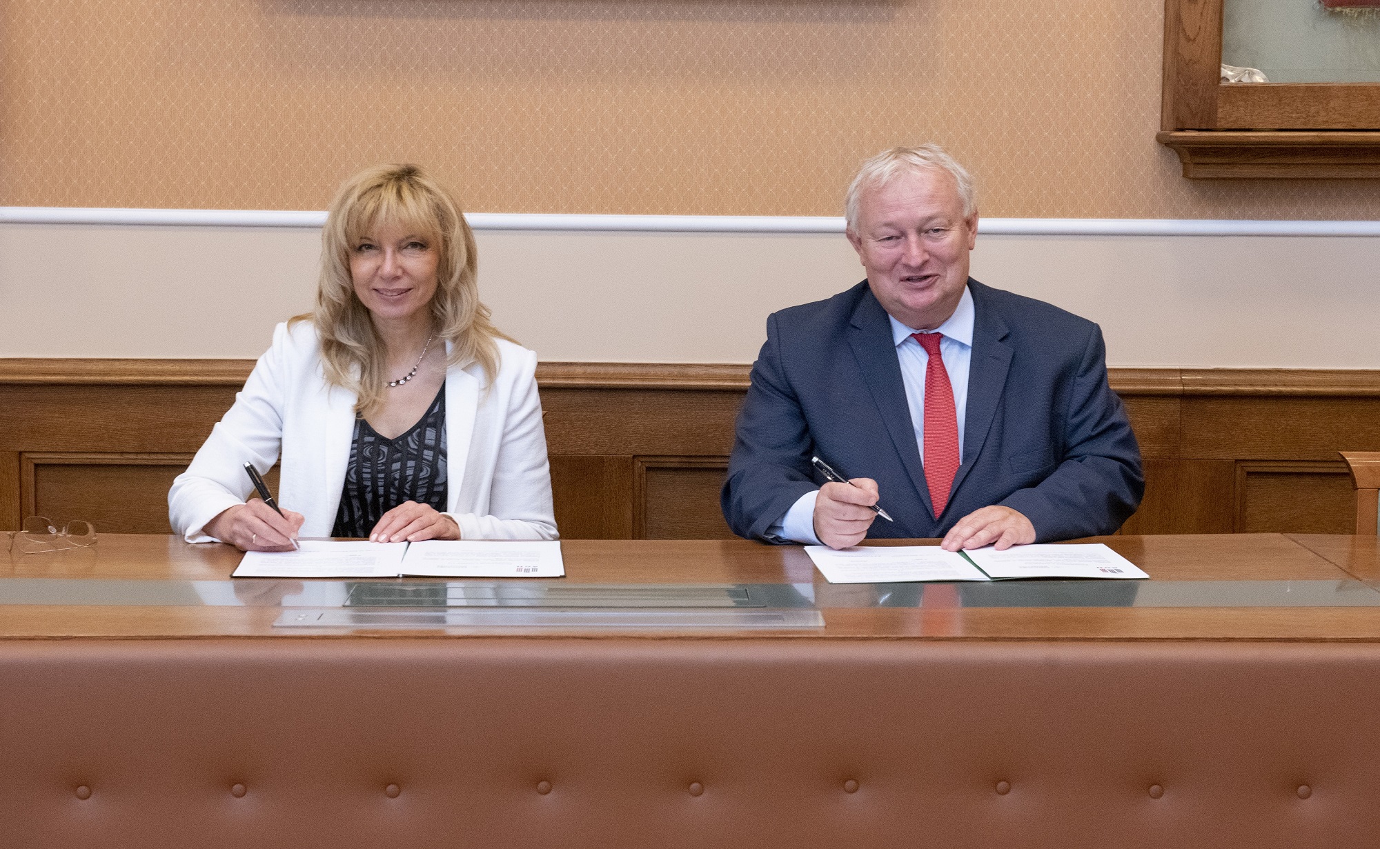 Na zdjęciu sygnatariusze umowy - siedzą za stołem, przed nimi dokumenty z umową, w dłoniach trzymają długopisy. Zdjęcie wykonane w sali konferencyjnej AGH.
