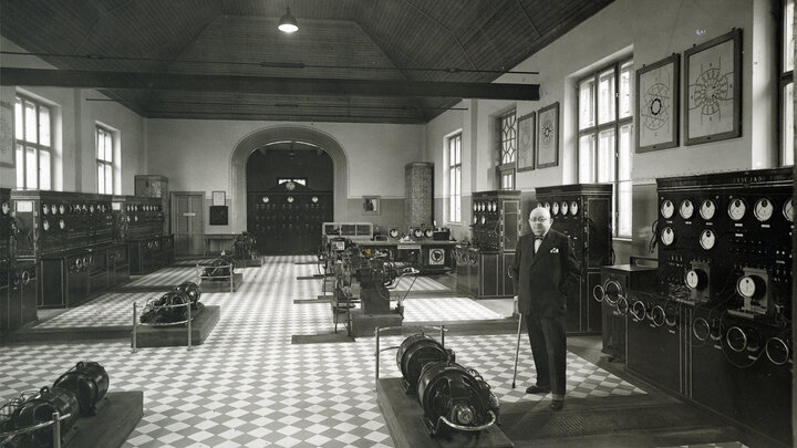 The interior of a electrical engineering production hall. Photo in black and white. A man in a suit and a cane standing on the right.