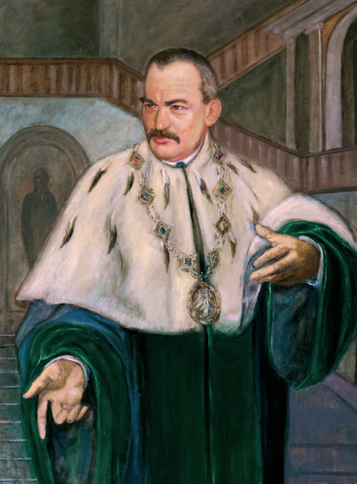 Portret przedstawiający Rektora Mirosława Handke stojącego w holu głównego budynku AGH (A-0). Rektor ma na sobie zieloną togę i gronostajowy kołnierz.