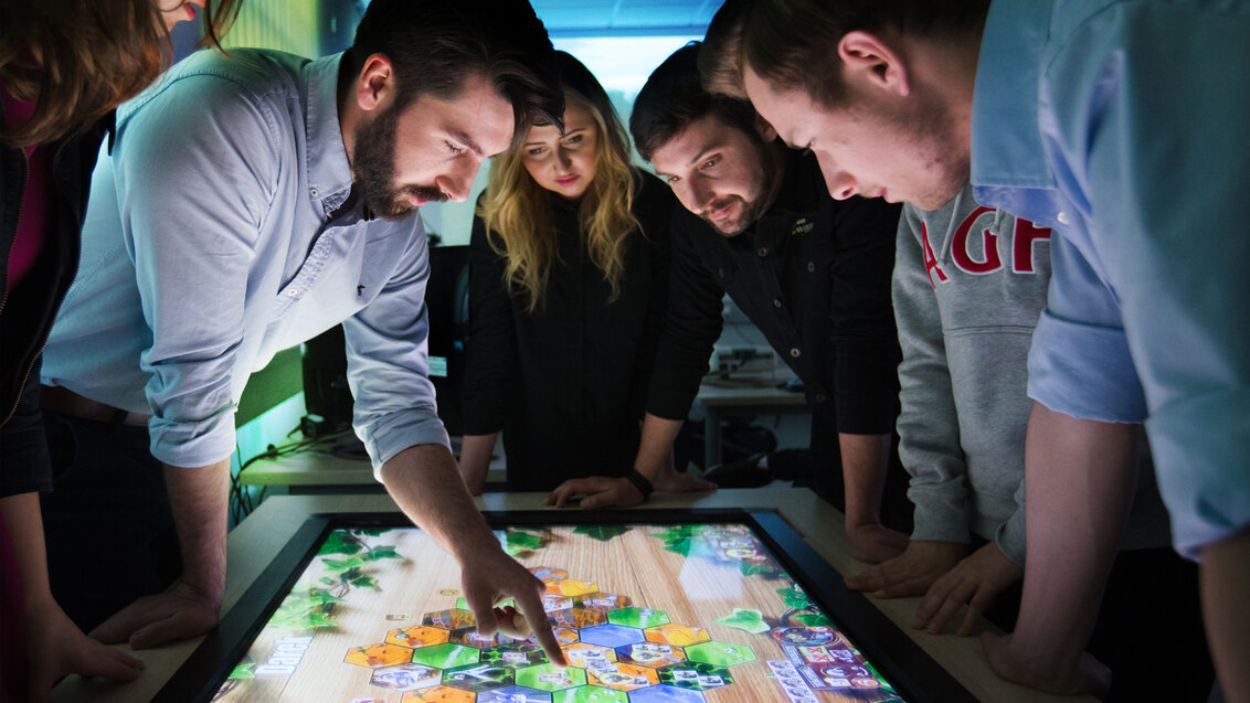A group of people around an interactive table with a game on.