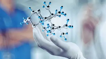 Dłoń w rękawiczce gumowej nad którą unosi się model budowy cząsteczki zbudowanej z kulek połączonych pręcikami.