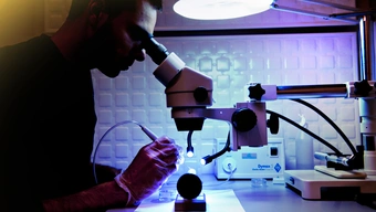 Młody człowiek w laboratorium bada obiekt pod specjalistyczny mikroskopem.