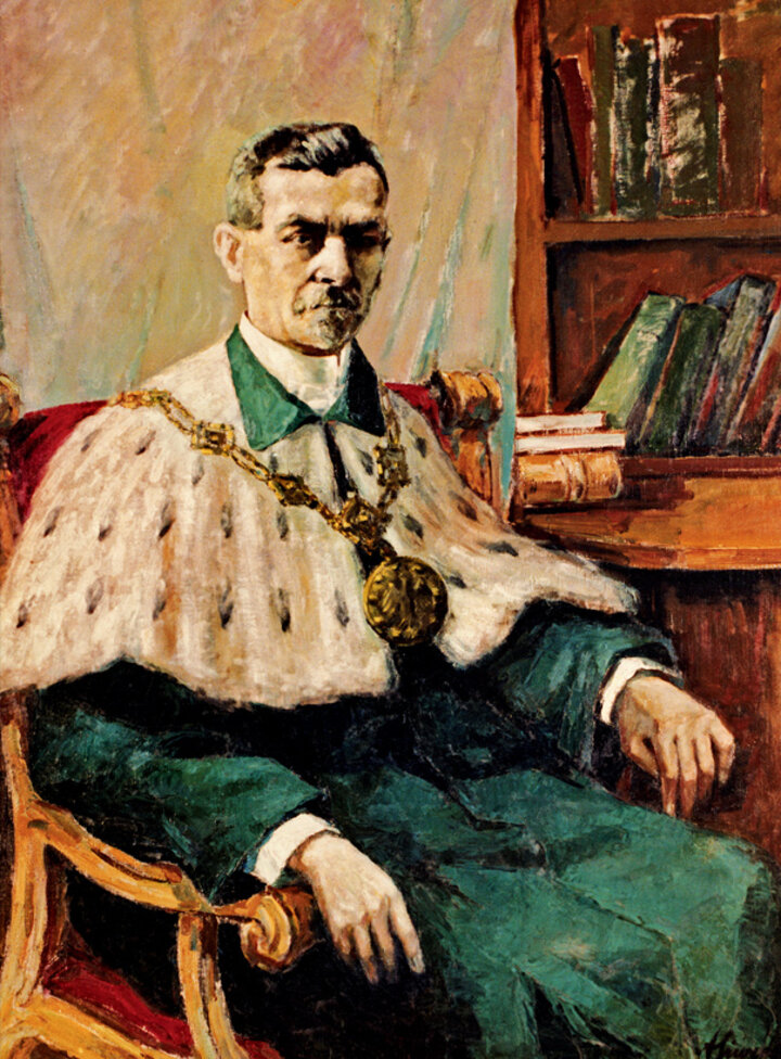 Portret Rektora Edmunda Chromińskiego. Rektor siedzi w fotelu, ma na sobie togę w zielonym kolorze, duży gronostajowy kołnierz oraz ozdobny łańcuch.