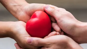 Zdjęcie prezentujące dłonie przekazujące sobie czerwone serce. 