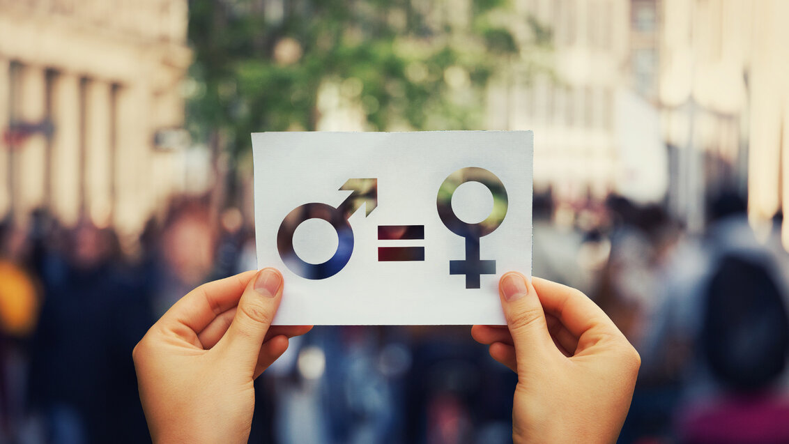 Hands holding a piece of paper with gender icons being equal
