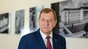 Image of the AGH University rector in front of a wall with black and white photographs of the university